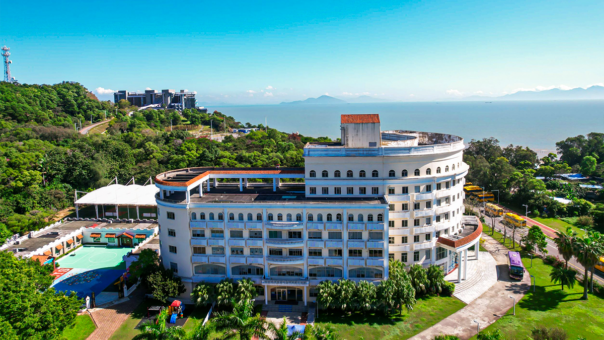Aerial view of Zhuhai International School, a large white circular building with lush greenery and the sea in the background.