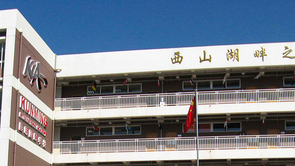 Front view of Kunming International Academy building showing bilingual signage and colorful international flag decorations.