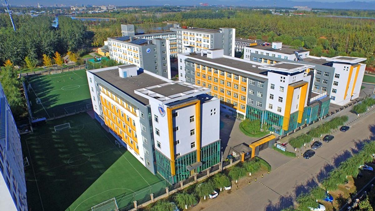 Aerial view of Beijing International Bilingual Academy campus with orange accents and green sports fields.
