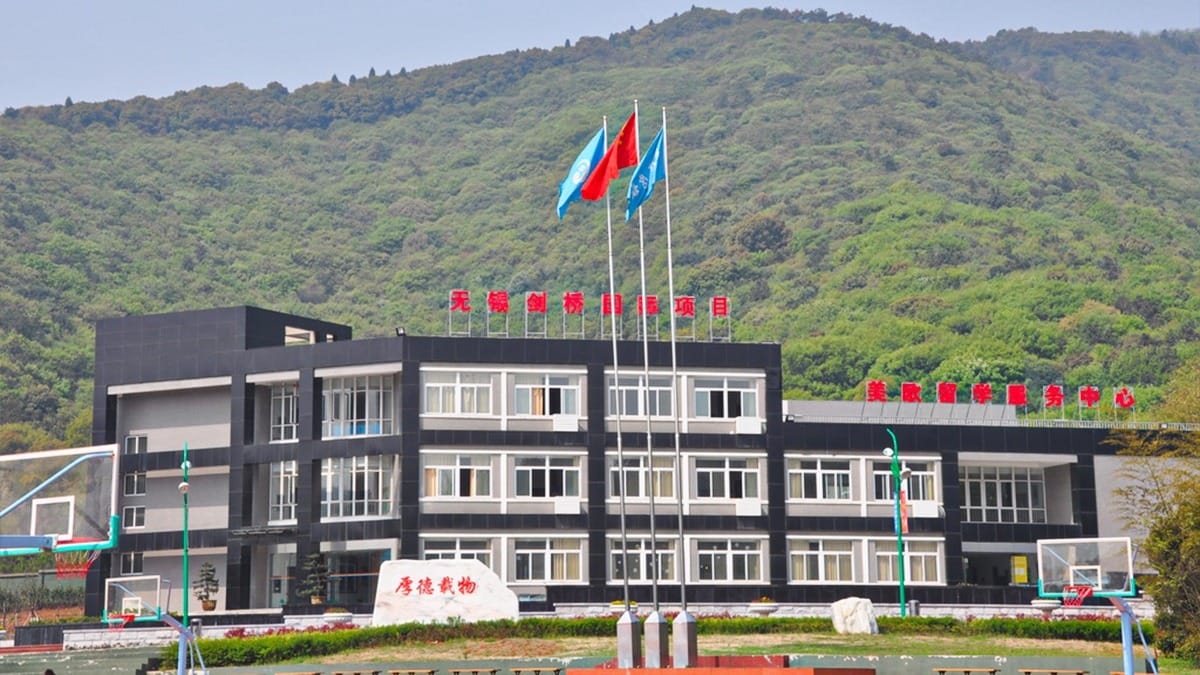 Wuxi Guanghua School building with flags and basketball courts against green hills