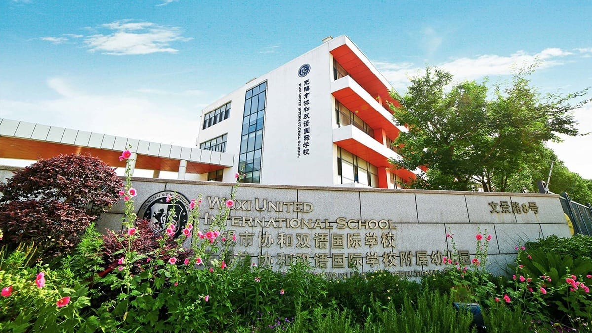 Wuxi United International School entrance sign with white and red buildings surrounded by flowers
